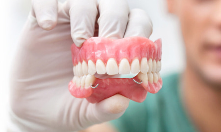 Стоматолог держит в руке съемные зубные протезы, фото Евродент