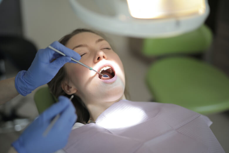 На изображении девушка лежит в стоматологическом кресле, доктор делает осмотр её зубов, фото Евродент